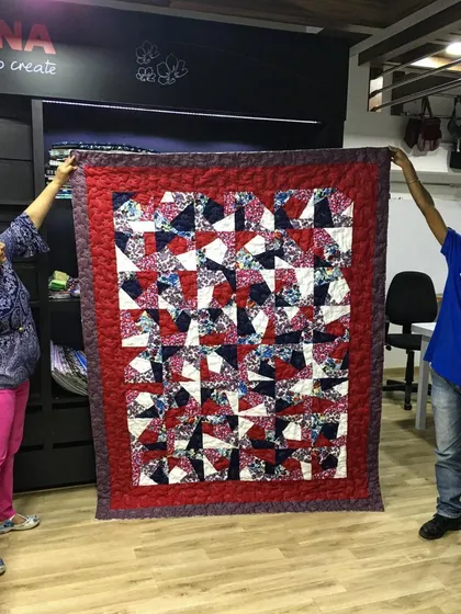 Two members of our team holding up a completed student project, a vibrant quilt with a complex geometric pattern.