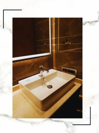 A rectangular vessel sink sits atop a marble counter, paired with a sleek, modern faucet. The large mirror behind it enhances the sense of space and light in the bathroom.