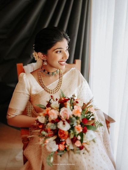 A serene portrait of the bride seated by a window, lost in a happy thought, her bouquet adding a splash of color.