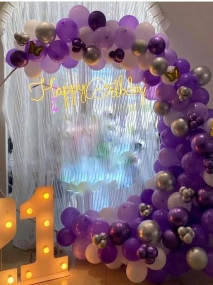 A 21st birthday celebration with a purple and silver balloon arch and marquee numbers.