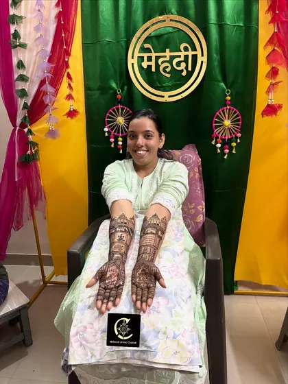 A happy bride showing her full-arm bridal mehendi. This design features detailed story-telling elements, including figures and traditional motifs, created with my homemade organic henna cones for a rich, dark stain.