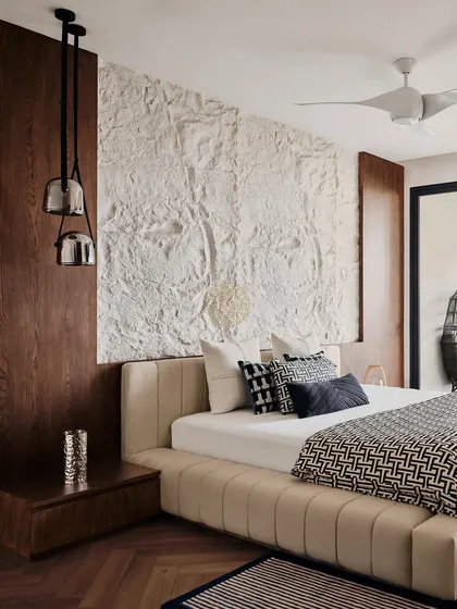 The master suite in this Bangalore home features a stunning textured white art panel behind the bed, flanked by dark wood panels. The herringbone oak flooring adds warmth and a classic touch.