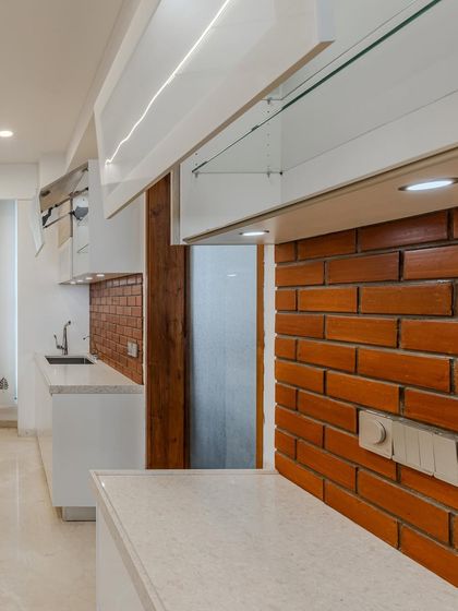 Another angle of the Ahmedabad kitchen, showing the 'Climber' style frosted glass cabinets. These lift-up units provide easy access and a modern touch, complemented by the warm brick backsplash.