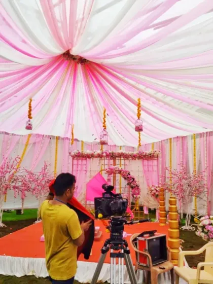 A view from behind the camera of a pink-themed mandap being set up, showing the extensive fabric draping and floral details.