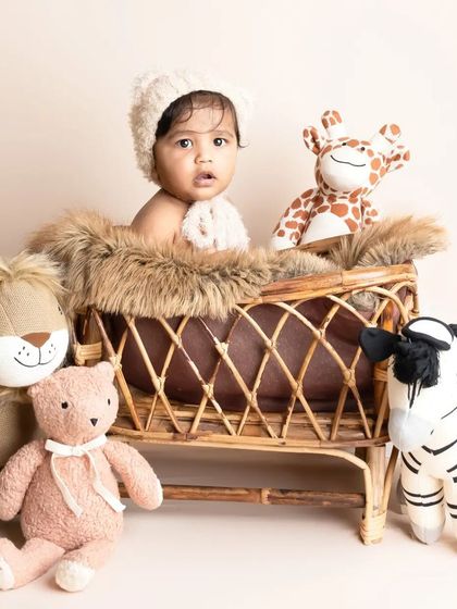 This little boy looks so sweet and curious in his rattan bassinet, surrounded by his animal friends. The combination of natural textures and soft toys is just perfect.