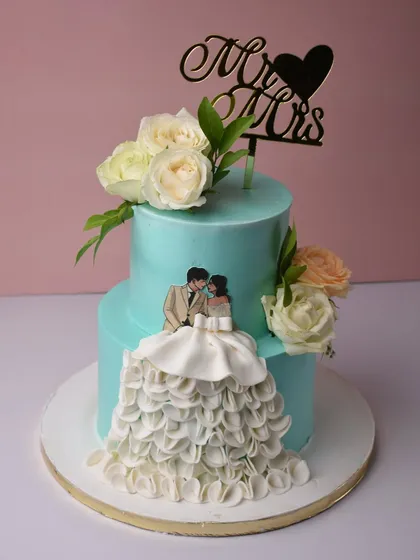 A cake for their pretty little beginnings. This two-tier design in a lovely turquoise shade features a hand-piped ruffled gown detail and a custom couple illustration, making it a unique and personal engagement cake.
