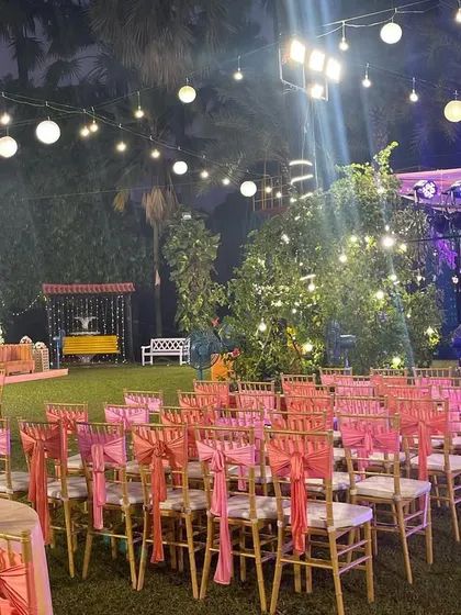 A view of the guest seating area for a reception, with the stage in the background. The pink chair sashes and warm lighting create a welcoming and festive atmosphere.