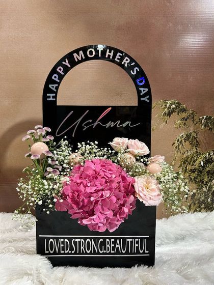 The "Posy Purity Purse" is where elegance meets creativity. This chic, black acrylic handbag-shaped box is filled with a beautiful arrangement of fresh hydrangeas and baby's breath, personalized with her name.