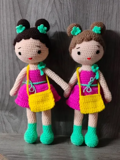 Two dolls in matching pink dresses with yellow bags. Their hair is tied up in cute buns.