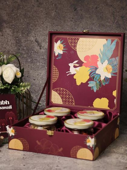 A rich magenta box with a beautiful floral and rabbit design. The satin-lined interior holds four jars of premium dry fruits, making it a royal gift for Diwali.