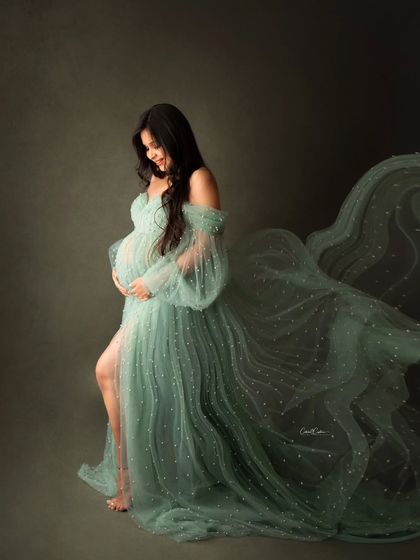 A gentle and serene portrait. The mom-to-be looks down at her bump, enveloped in the soft, flowing fabric of her green gown.