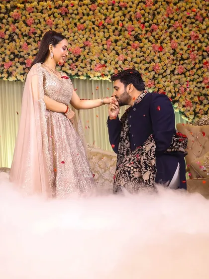 A classic, romantic gesture. The groom-to-be kisses his fiancée's hand during their engagement ceremony on a beautifully decorated stage.