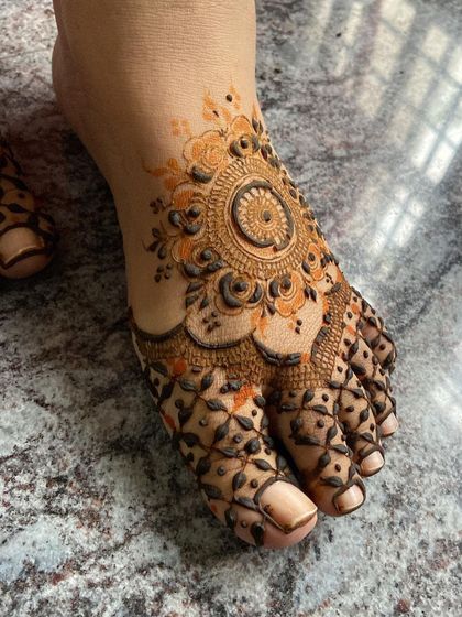 A close-up of a foot mehendi design with a central mandala and netted pattern on the toes.