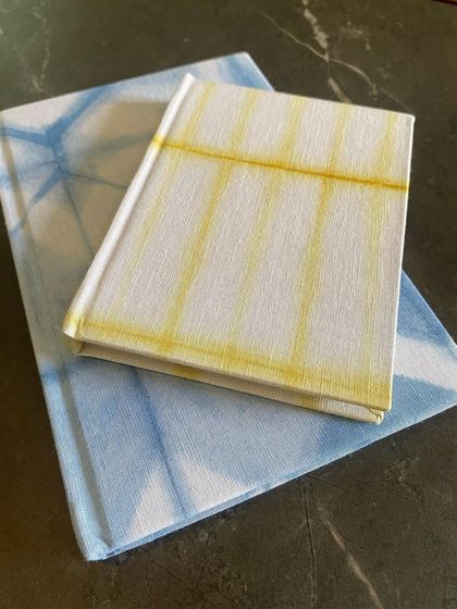 A close-up of the indigo and marigold dyed notebooks. The beautiful patterns and hardcover design make them a stylish and sustainable choice for your notes and thoughts.