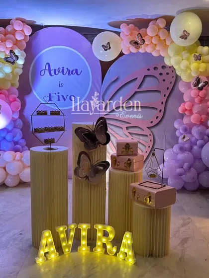 A magical butterfly theme for a 5th birthday. The setup includes a large butterfly wing backdrop, pastel balloon garlands, and a light-up number '5'.