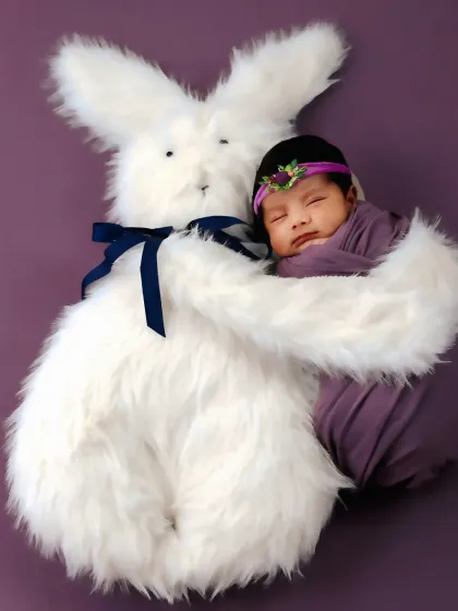 A sleeping newborn gets a hug from a large plush bunny, creating an image of pure sweetness and comfort.