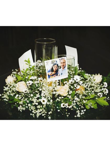 A personal touch for a table centerpiece. We incorporated a small photo of the couple into this delicate arrangement of baby's breath and white roses.