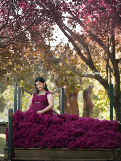 A stunning solo portrait in a wine-colored ruffled gown, set against a backdrop of trees with autumn leaves.