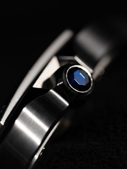 A macro detail of the faceted blue synthetic spinel set into the crown. This is a signature Cartier detail that adds a subtle touch of color and luxury.