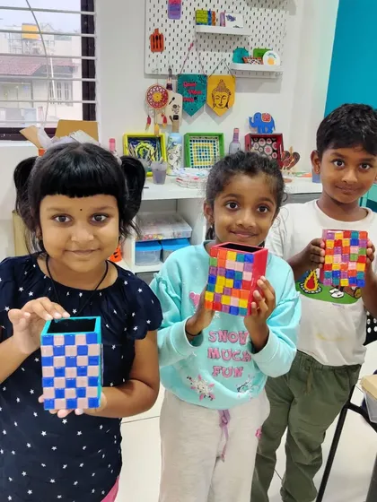 Three young friends proudly present their finished mosaic pen stands after a fun group art session.