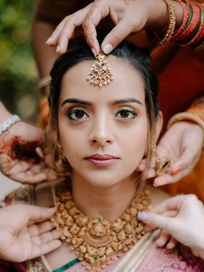 The final touches. This powerful image captures the hands of loved ones helping the bride with her jewelry, a beautiful symbol of family and support.