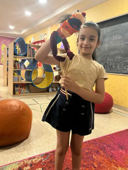This student proudly displays her unique rod puppet, ready for the final performance. Each puppet has its own personality, just like its creator.