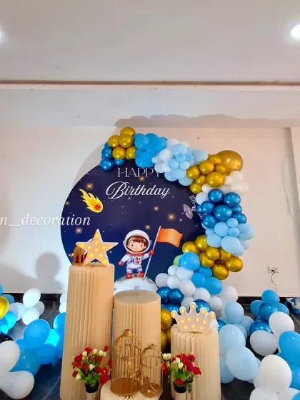A full view of the space-themed birthday decoration with a circular backdrop featuring an astronaut on the moon, surrounded by a blue, white, and gold balloon garland.