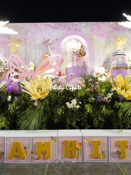For this enchanted forest stage, I used a dense arrangement of flowers and greenery at the base to create the feeling of a real forest floor. The setup is completed with custom name blocks, large paper flowers, and glowing butterfly props.