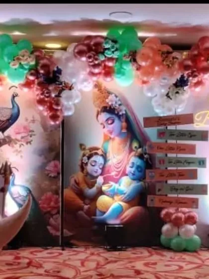 A beautiful baby shower stage with a Krishna theme. The decor includes a large moon prop, character cutouts, and a balloon arch in pastel colors.