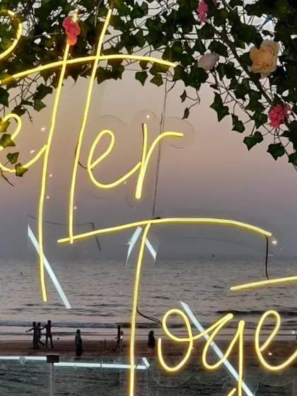 A close-up of the 'Better Together' neon sign, framed by a floral arch. This detail, set against the evening sky and the beach, became a favorite photo spot for the couple and their guests.