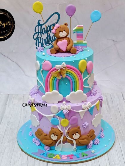 A charming two-tier pineapple cake for a first birthday. The design features fondant teddy bears, a rainbow, and colorful balloons in a soft pastel palette.