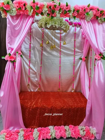 A lovely pink-themed Ganpati mandap. The satin drapes, floral borders, and hanging bells create a soft and pretty space to welcome Bappa.
