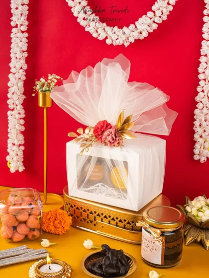 A slightly different angle of the premium white Diwali hamper, set against a vibrant yellow background to make the colours pop.