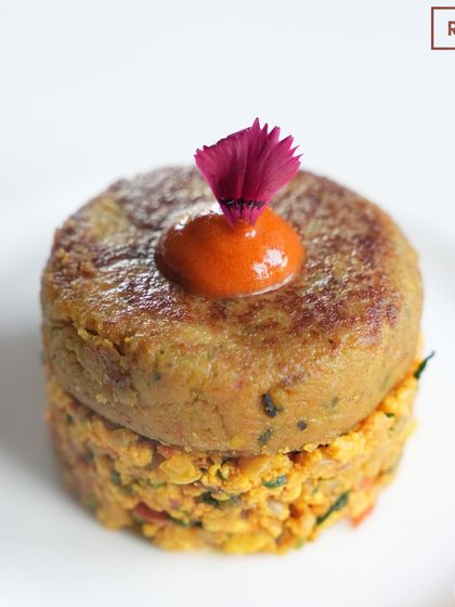 A studio shot of the vegetarian Shami Kebab, highlighting its perfect form and the delicate edible flower garnish. It's a star of our Chef's Tasting Menu.