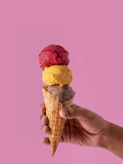 A triple-scoop ice cream cone held against a bright pink background. This is a fun, colorful, and eye-catching shot perfect for summer.
