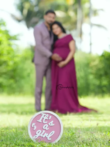 A close-up of a gender reveal prop that says "It's a girl!", with the happy couple blurred in the background.