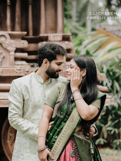 A close-up, intimate portrait of a couple in traditional attire, surrounded by greenery.