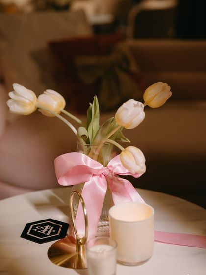A minimalist centerpiece with white tulips in a glass vase, tied with a playful pink satin bow.