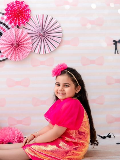 A sweet, seated portrait of a girl in a pink sequin dress, her happy smile lighting up the room.
