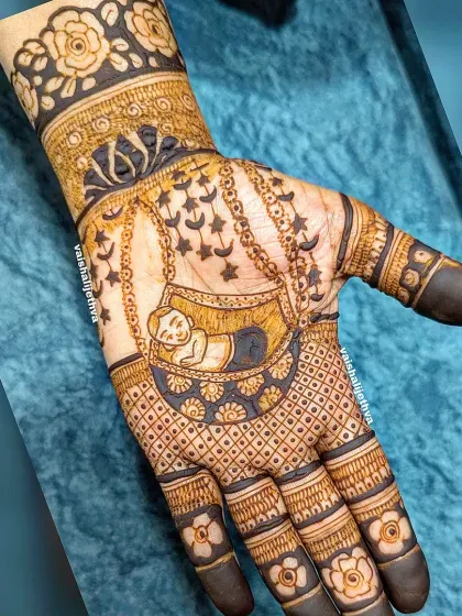 A sweet and simple baby shower design. This mehndi features a baby sleeping in a cradle, surrounded by delicate hanging charms and floral patterns.