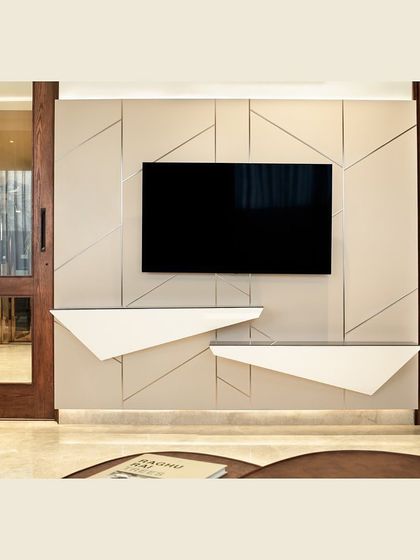 This statement TV unit features a geometric, paneled design with integrated, angular shelves. The minimalist, off-white tone allows the sculptural form to stand out, adding character to the room even when the screen is off.