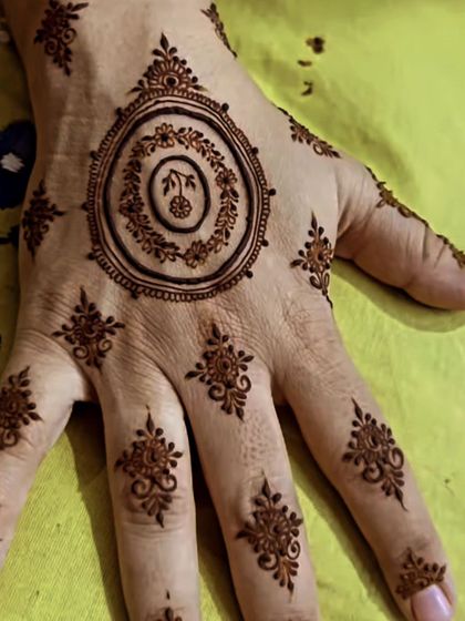 Here, the modern circular mandala is complemented by small, scattered butis across the fingers and hand. This adds a bit more detail while keeping the overall feel light and minimalist.