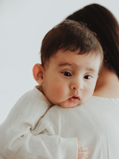 A quiet and contemplative moment from a baby milestone session. The baby peeks over mom's shoulder, creating a simple yet powerful portrait.