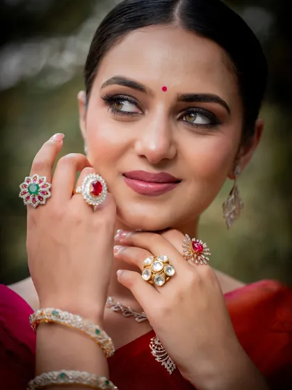 A close-up on the model's hands, showcasing a stunning collection of diamond, ruby, and emerald rings.