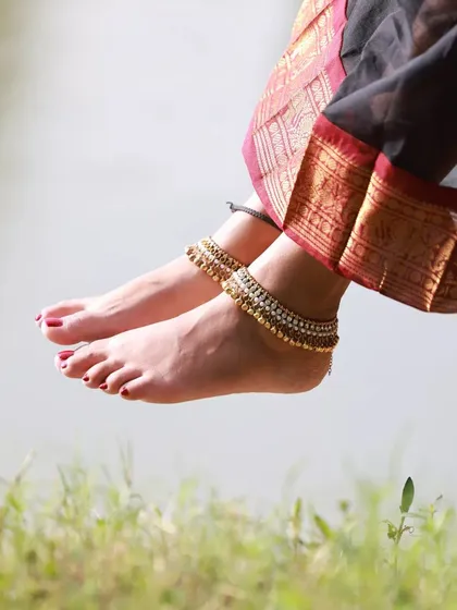 A close-up shot focusing on the model's feet and anklets, dangling over the grass. This kind of detail shot adds an artistic and sensory element to the photo series.