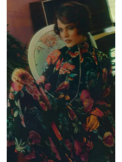A close-up portrait from 'The Wait'. The model's direct gaze and the rich floral patterns of her outfit create an intimate and contemplative mood, drawing the viewer into her emotional state.