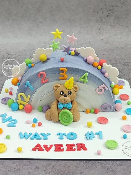 A colorful half-birthday cake to celebrate 6 months. This rainbow-shaped cake is decorated with a teddy bear, numbers, and buttons, marking the "Way to #1".