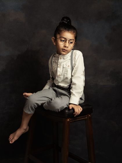 A cool and contemplative portrait of a young boy. The vintage-style glasses and his relaxed pose give this image a unique and thoughtful vibe.
