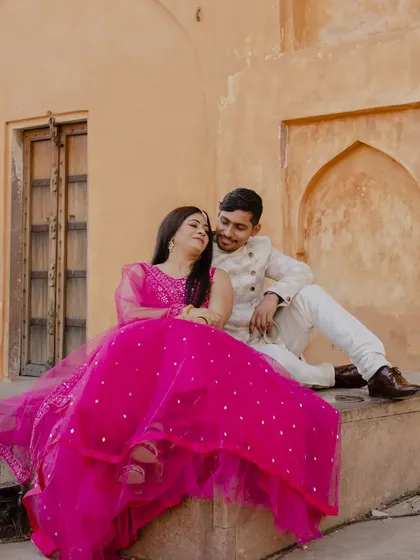 A quiet, seated pose that feels both intimate and grand. The warm tones of the fort walls and the bride's vibrant pink dress create a beautiful color harmony.