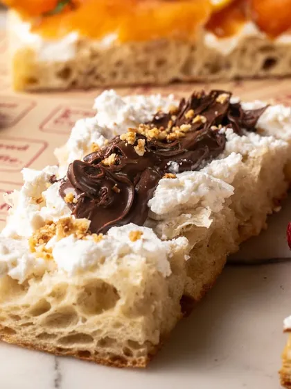 A close-up of a focaccia slice with ricotta and chocolate spread. The detail shot highlights the creamy and rich textures.